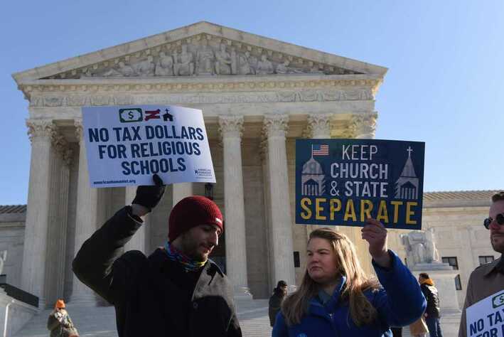 Two protesters standing in front of the Supreme Court. One holds a sign saying 