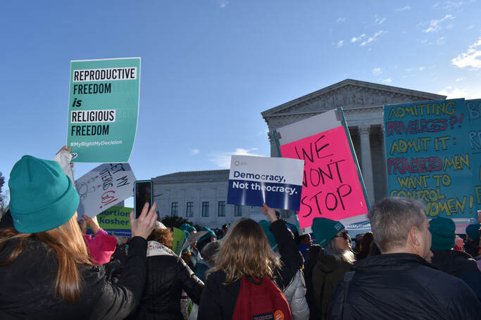 Protesters stand outside the Supreme Court. They hold signs saying 